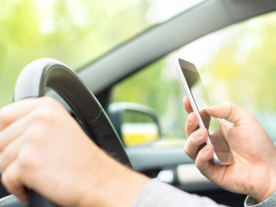 Man using smartphone while driving. Driver texting and sending sms and using mobile phone in car. Writing and typing message with cellphone in vehicle.